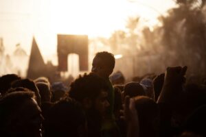 Dramatic photo of a child in a crowd at a Karbala event with sunset light.